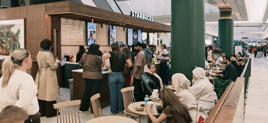 Starbucks kiosk trading with customers queuing and seating beside the green fluted columns