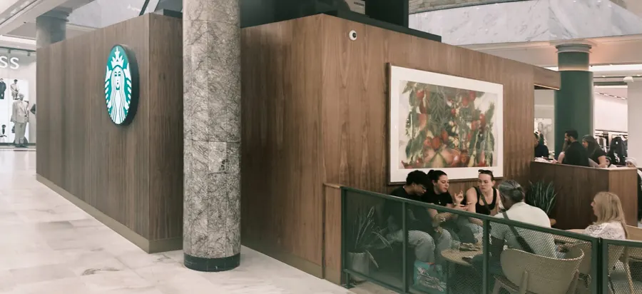 Walnut-clad rear elevation of the Starbucks kiosk with illuminated logo and framed artwork
